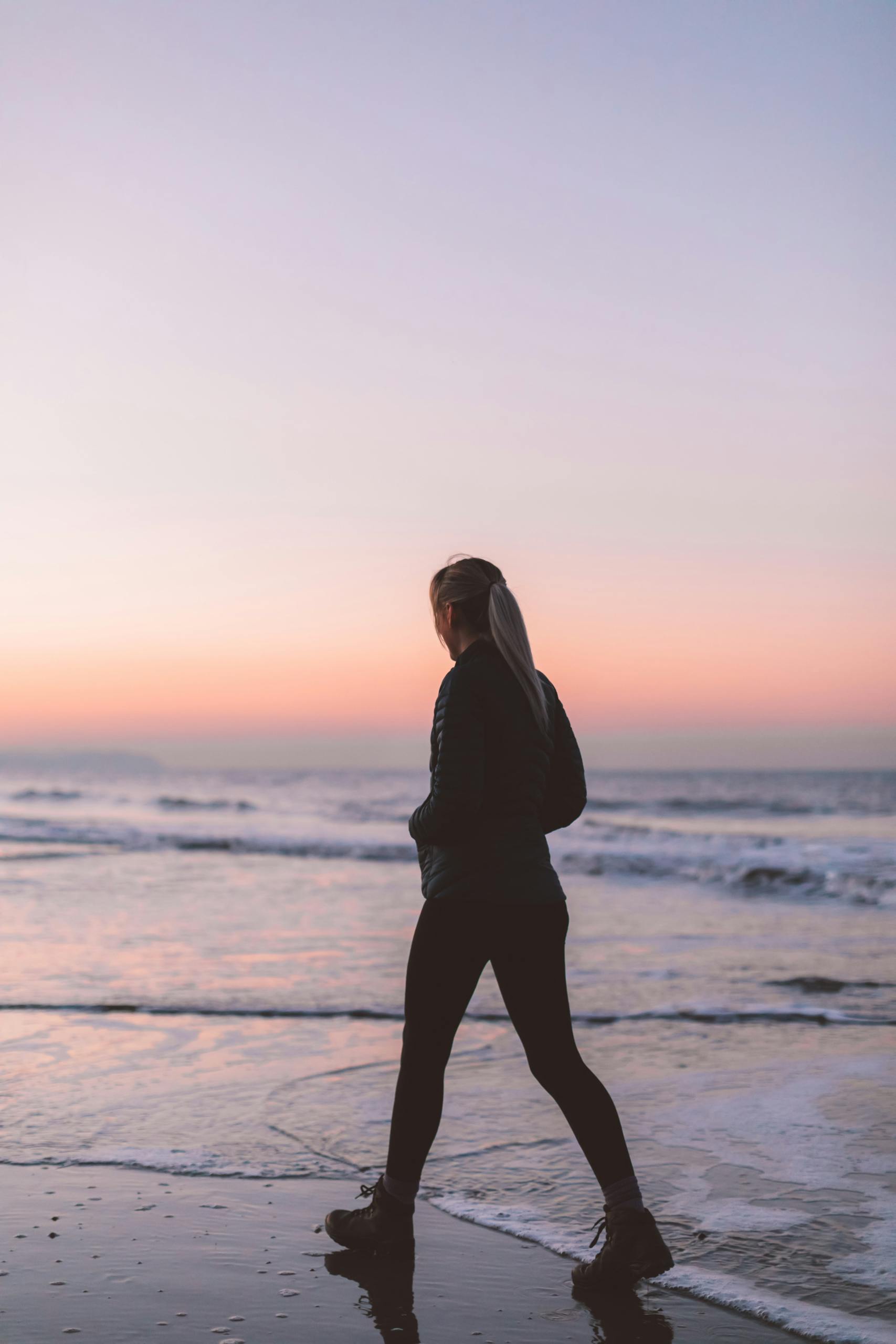 A woman walks along the beach at sunset, enjoying the tranquil ocean scenery.
