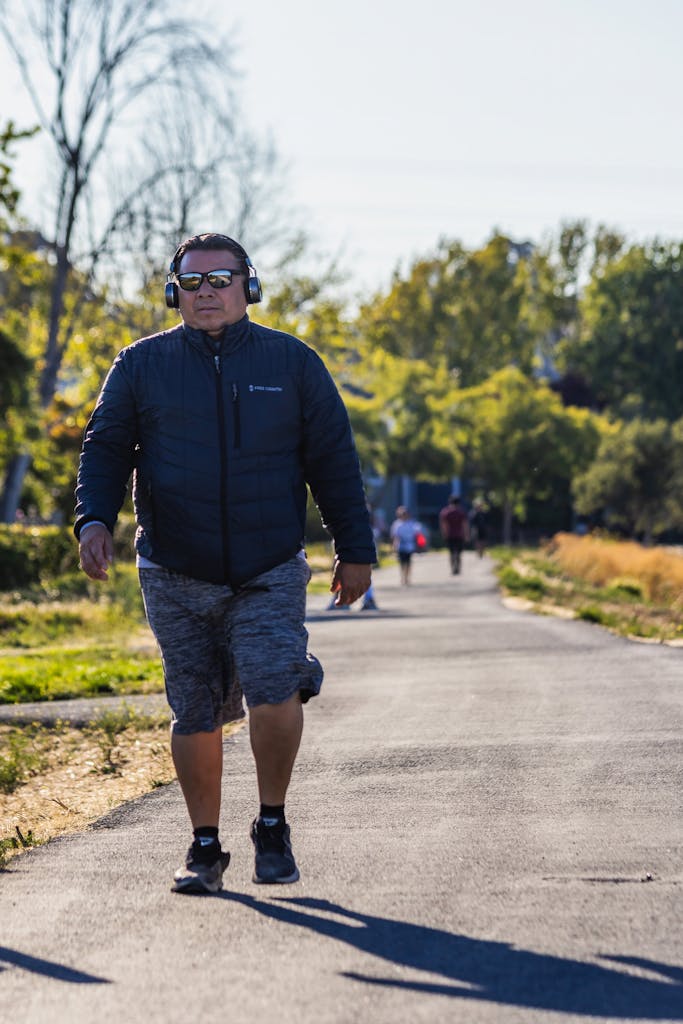 Adult man enjoying a walk with headphones in a sunny park setting.