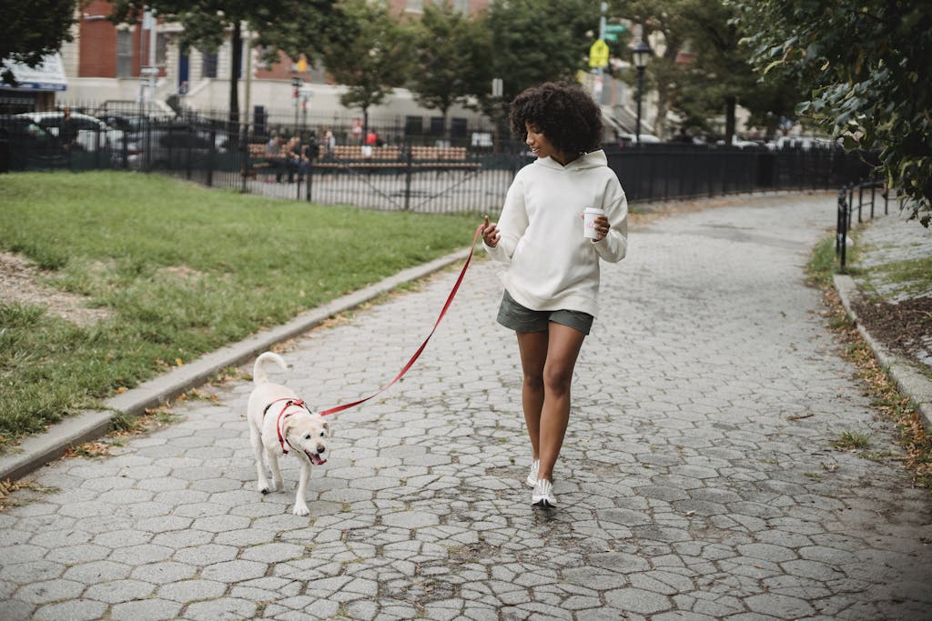 Woman strolling with her dog on a city sidewalk, enjoying a to-go coffee.